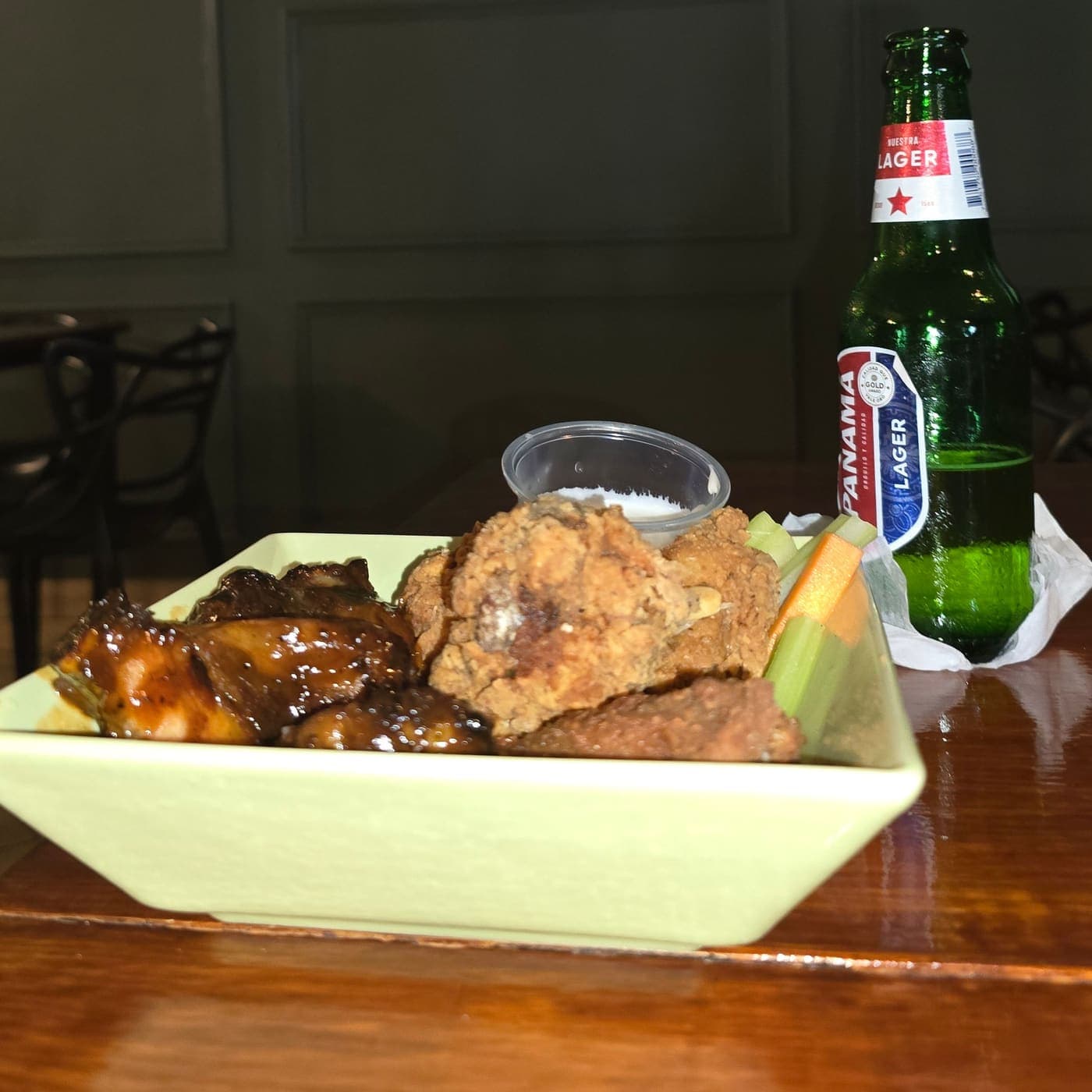 Picada de alitas con salsa y bastones de apio y zanahoria, junto a una cerveza Panamá, en una mesa de El Green Room