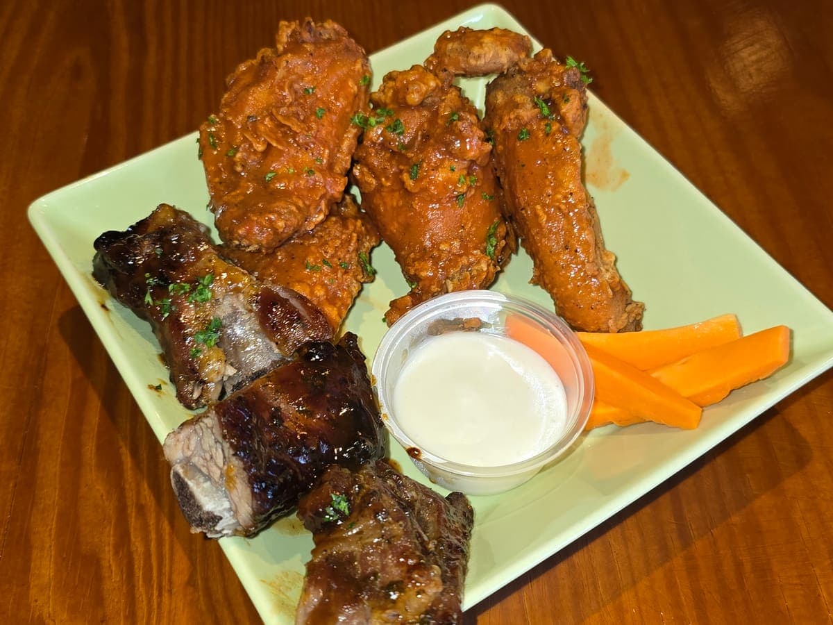 Rock n Bones: costillas BBQ y alitas Buffalo con zanahoria y salsa ranch, sobre una mesa de madera